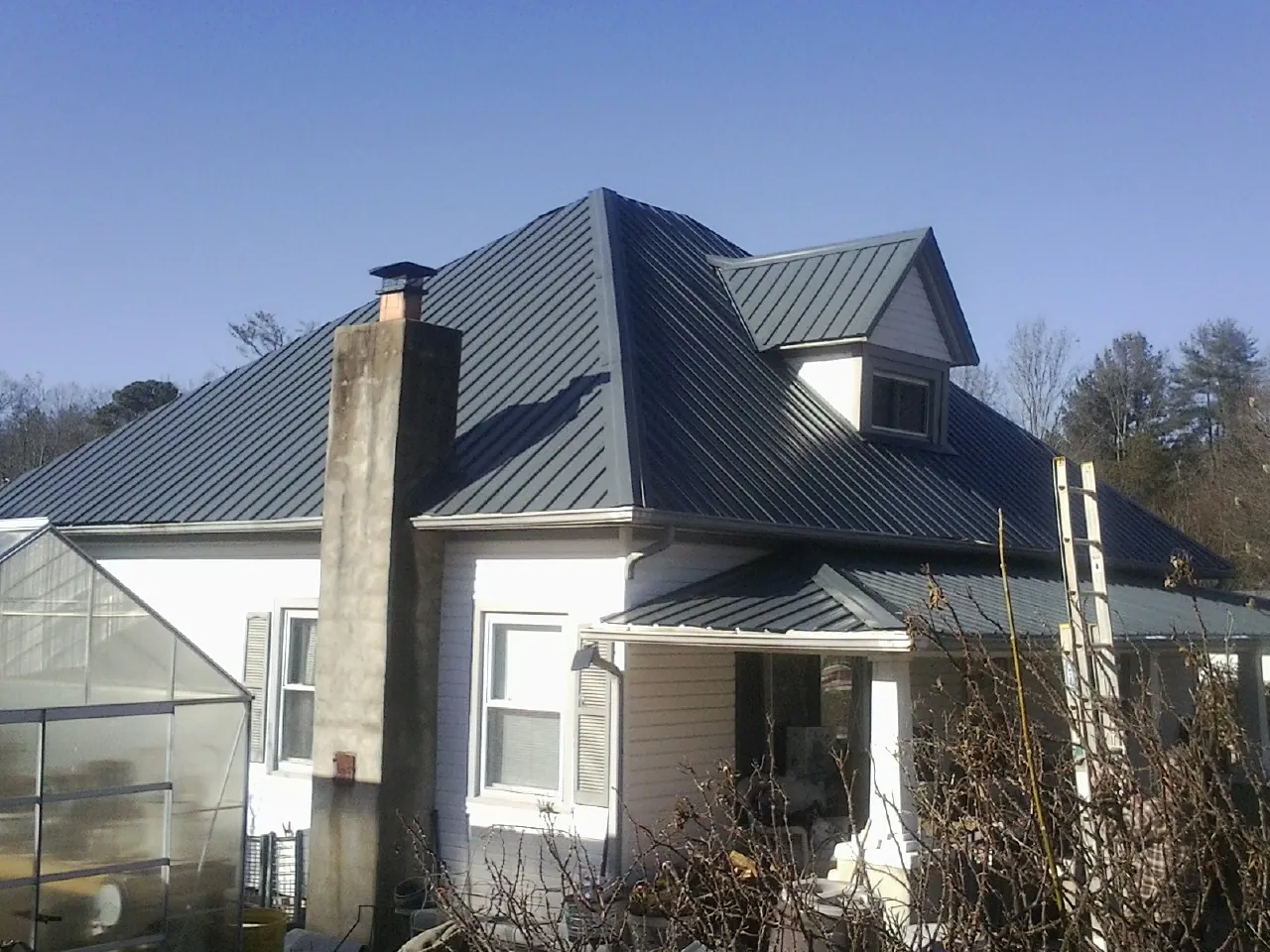 Dark blue standing seam metal roof on a white farmhouse with dormer — Slate & Tile Roof Repair by Roofing Brothers in Brookwood