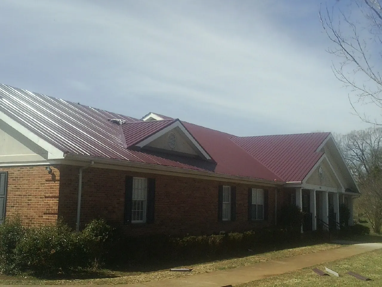Red metal roof with gabled entries on a long brick building, from a Hail Damage Roof Repair job in Brookwood
