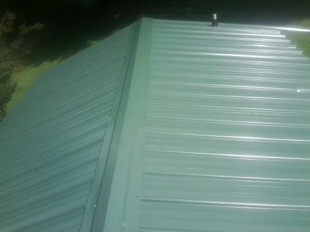 New green metal panels meeting at the ridge of a roof — Flat Roof Repair work by our crew in Brookwood