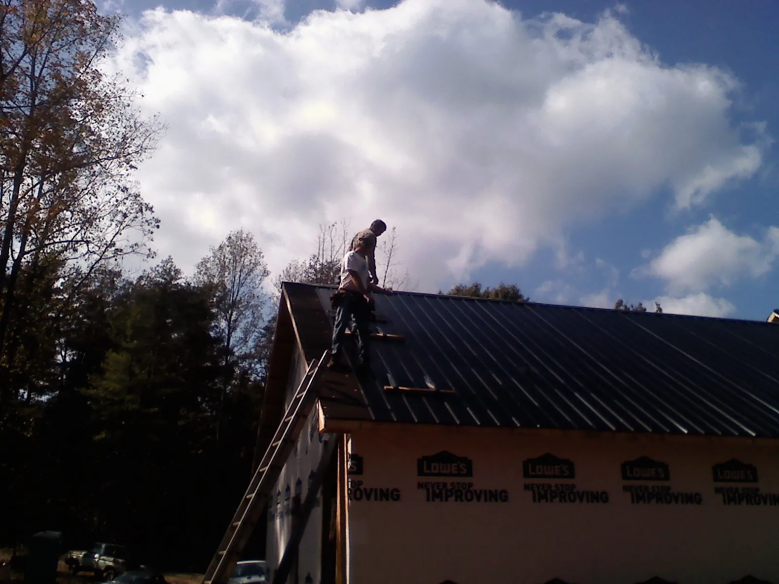 Roofer fastening dark metal panels high against a cloudy sky, from a Roof Inspection job in Brookwood