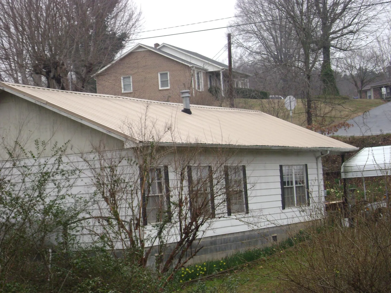 Tan metal roof on a white sided house set into a hillside — Commercial Roofing by Roofing Brothers in Brookwood
