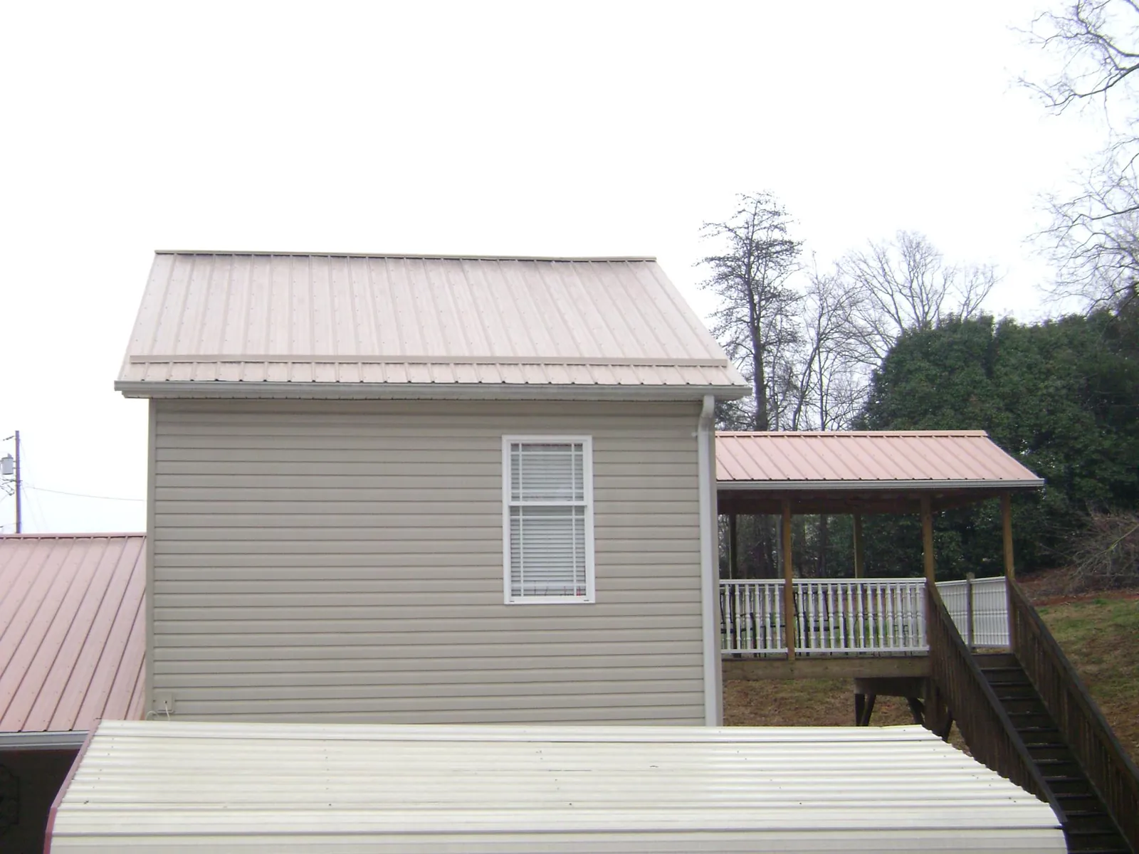 Tan metal roofs on a two story addition and attached porch, from a Roof Replacement job in Brookwood
